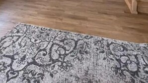 Amplia sala de estar con una escalera de madera, una cocina con armarios blancos y una alfombra estampada en el suelo.