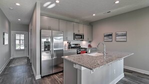 A modern kitchen with stainless steel appliances, a granite countertop island, and recessed ceiling lighting.