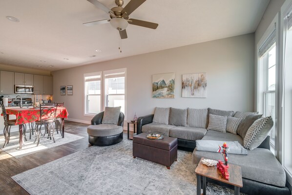 A spacious living room with a gray sofa, a dining area with a red tablecloth, and a kitchen in the background. - Lovely Bowling Green Home, 10 Mi to Downtown! (Bowling Green)