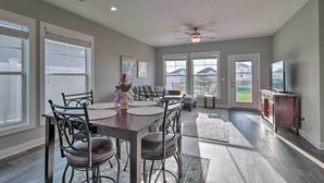 A spacious dining area with a dark wooden table and metal chairs, large windows, and a ceiling fan.
