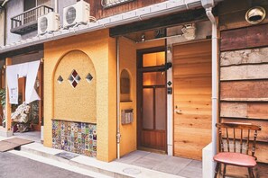 A building with a tiled entrance, a wooden door, and a balcony with air conditioning units.