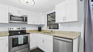 Une cuisine moderne avec des meubles blancs, des appareils en acier inoxydable, un plan de travail en granit et une fenêtre offrant une belle vue.