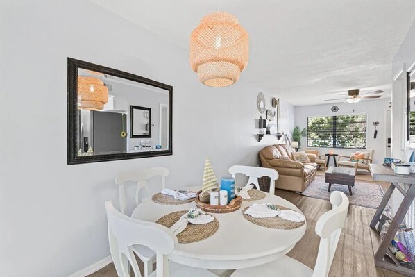 A dining area with a round table, white chairs, and a hanging rattan light fixture.