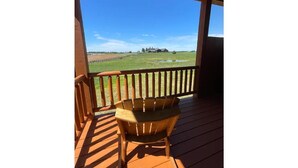 A wooden deck with a view of a rural landscape, including a house and fields.