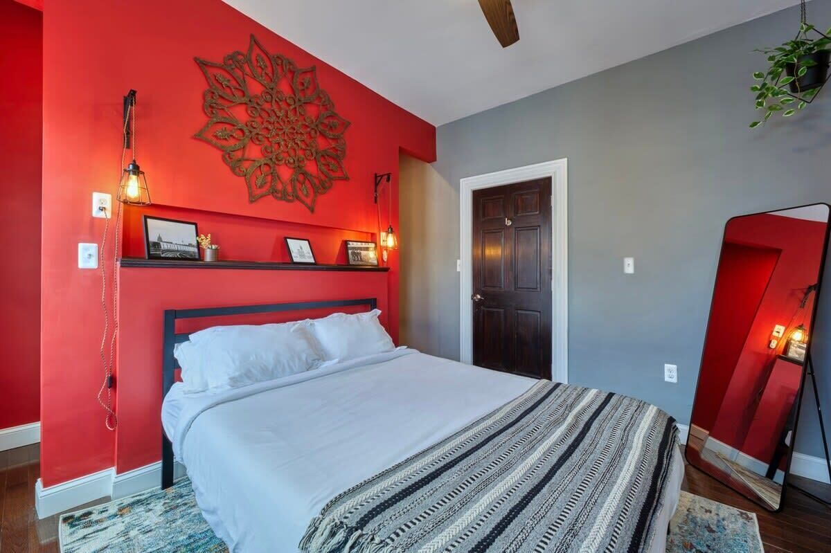 Une chambre à coucher avec un lit, un mur d’accent de couleur rouge, un élément décoratif mural, un miroir et une porte.