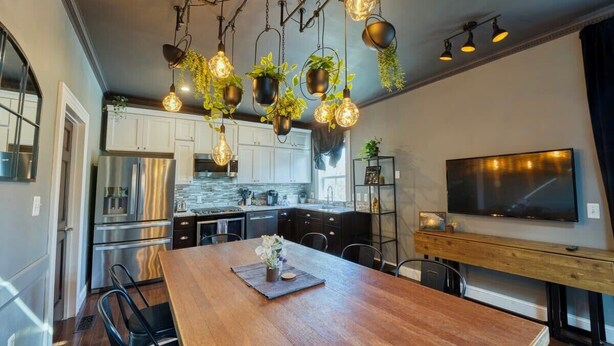 Una cocina moderna con plantas colgantes, una mesa de comedor de madera y un televisor de pantalla plana grande.
