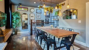 Un comedor con una mesa de madera y sillas negras, rodeado de plantas y cuadros en las paredes.
