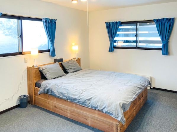 A bedroom with a wooden bed, two bedside lamps, and a window with curtains.