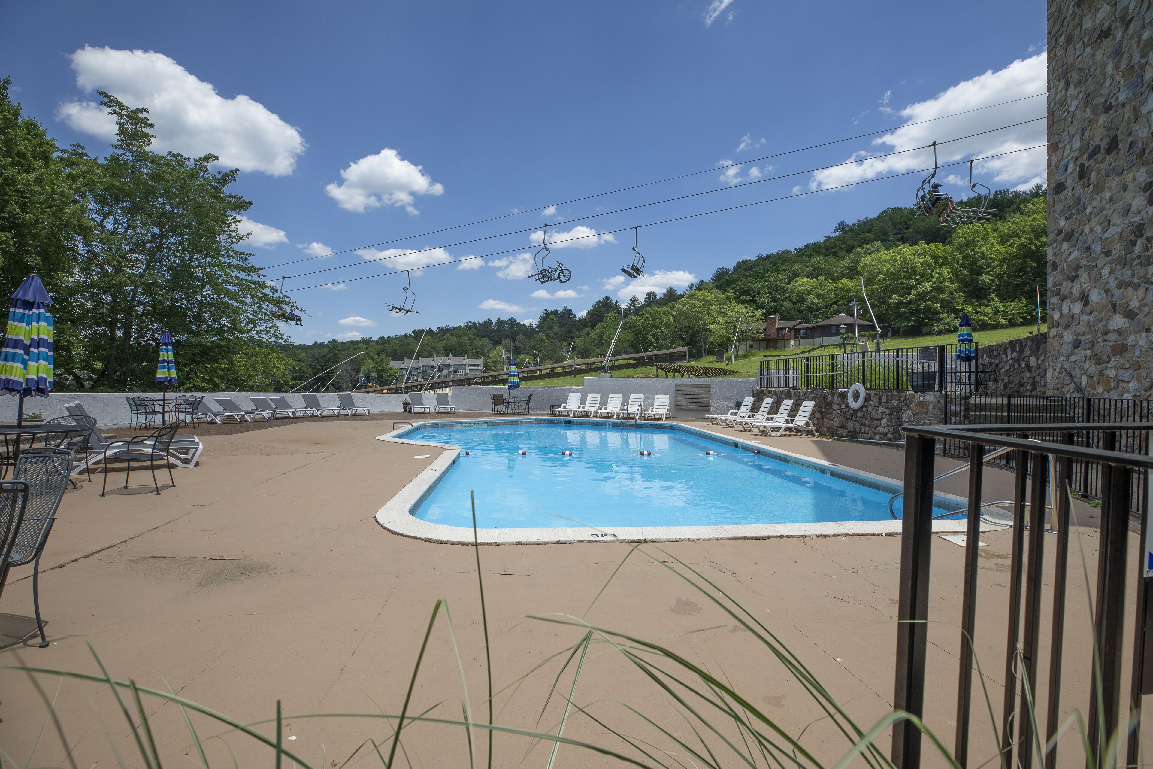 A swimming pool with lounge chairs and a ski lift in the background.