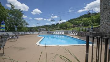 A swimming pool with lounge chairs and a ski lift in the background.