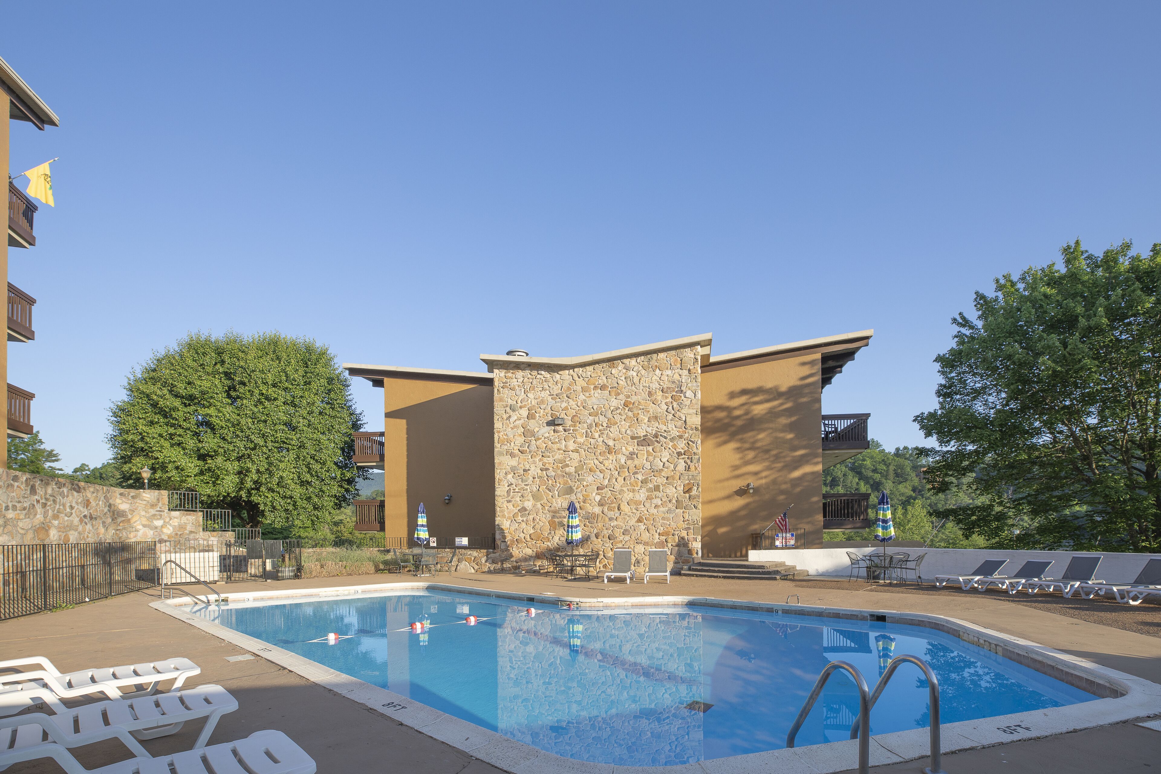 A swimming pool with lounge chairs and umbrellas, surrounded by stone walls and a clear blue sky.