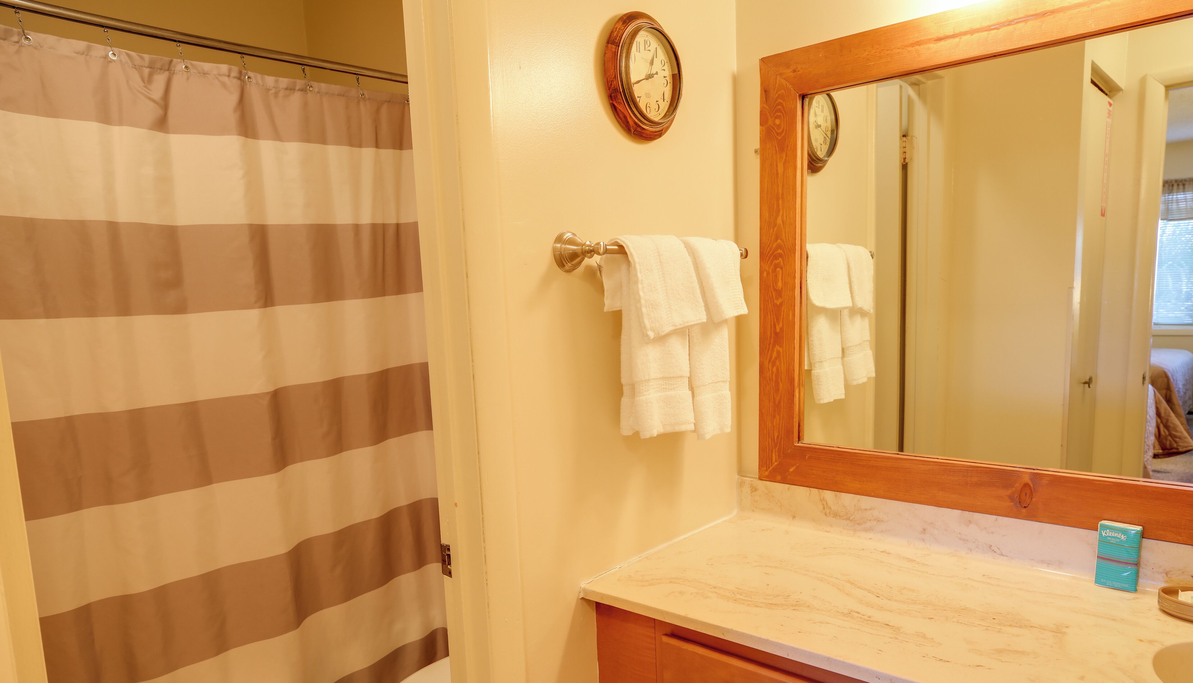 Une salle de bain avec un rideau de douche à rayures, un miroir encadré en bois et des serviettes blanches suspendues à un porte-serviettes.