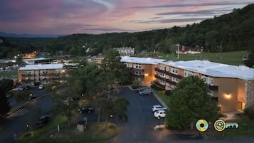 An aerial view of a multi-story building complex with parking areas, surrounded by greenery and a hilly landscape.