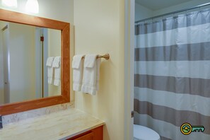 A bathroom with a marble countertop, a wooden-framed mirror, and a striped shower curtain.