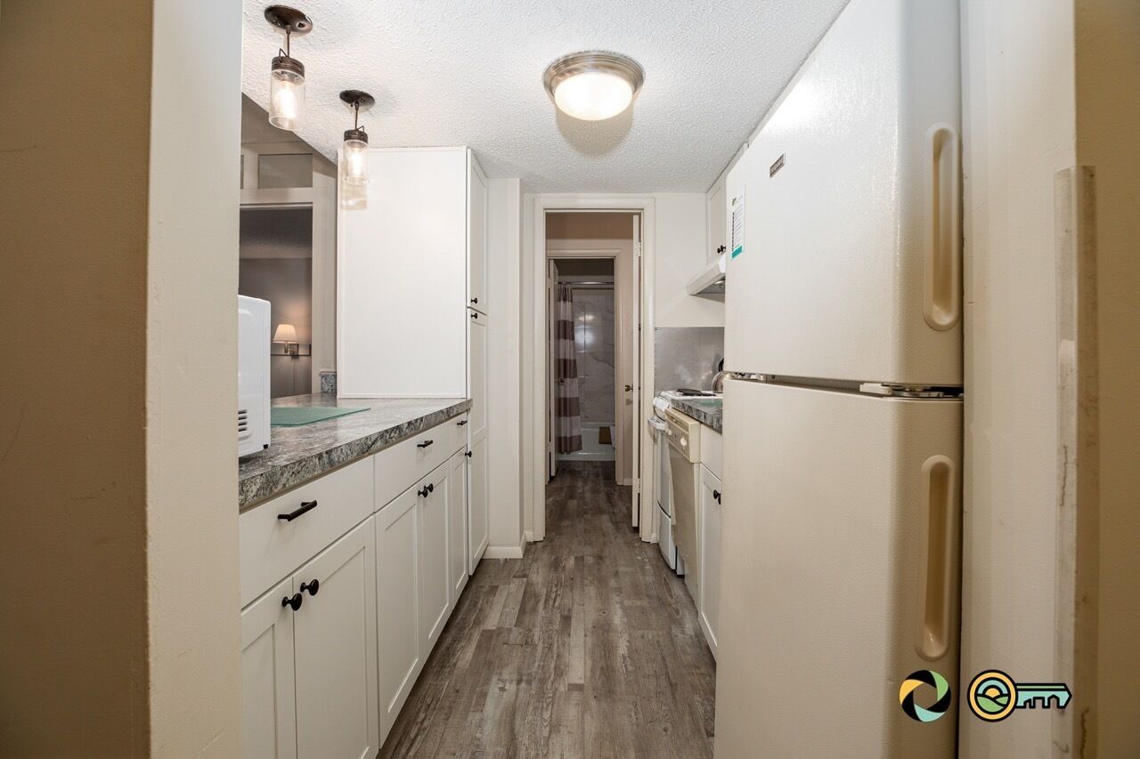 A narrow kitchen with white cabinets, a refrigerator, and a countertop.