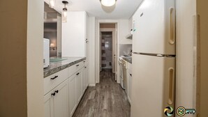 Una cocina estrecha con armarios blancos, un refrigerador y una encimera.