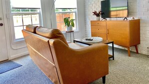 Een woonkamer met een leren bank, een houten kast, een televisie en een plant.