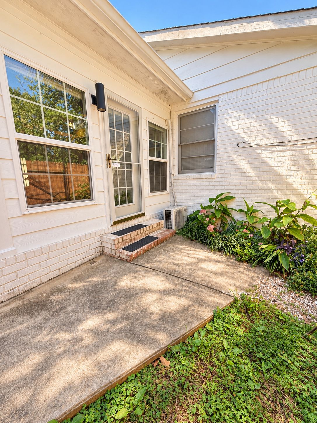 A residential house with a front porch, a brick foundation, and a small garden area.