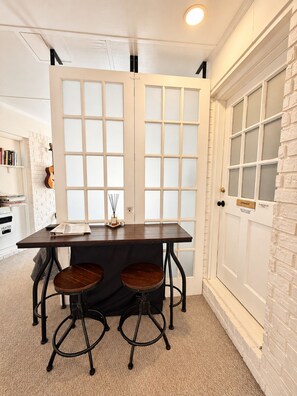 A dining area with a table and two stools, a white door with frosted glass panels, and a brick wall. - Toadhaus - Modern Studio Suite in Athens GA Residential UGA safe private patio (Athens)