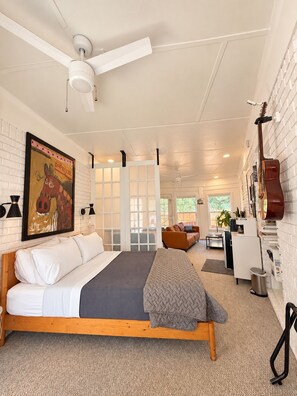 A modern bedroom with a wooden bed, a ceiling fan, a guitar, and a painting on the wall. - Toadhaus - Modern Studio Suite in Athens GA Residential UGA safe private patio (Athens)