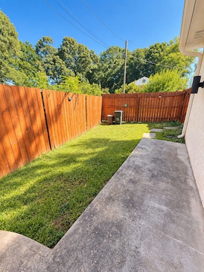 A backyard with a wooden fence, a concrete patio, and a grassy area. - Toadhaus - Modern Studio Suite in Athens GA Residential UGA safe private patio (Athens)