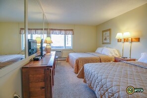 A hotel room with two beds, a desk with a television, lamps, and a window with curtains.