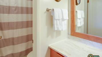 A bathroom with a striped shower curtain, a white toilet, a marble sink with a wooden cabinet, and two wall clocks.