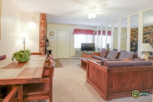 A living room with a wooden sofa, a TV, and a dining area with a table and chairs.