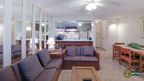 A living room with a sofa, coffee table, and a dining area with a table and chairs. There is a kitchen area in the background with a refrigerator, microwave, and stove. - Ski/MTB/Golf Condo (#117) - Slope side | Ski slope & Resort views | Walk-in access! (Basye)