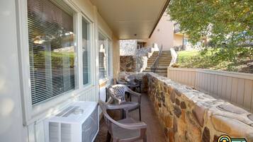 An outdoor patio with a stone wall, a staircase, and a covered seating area with chairs.