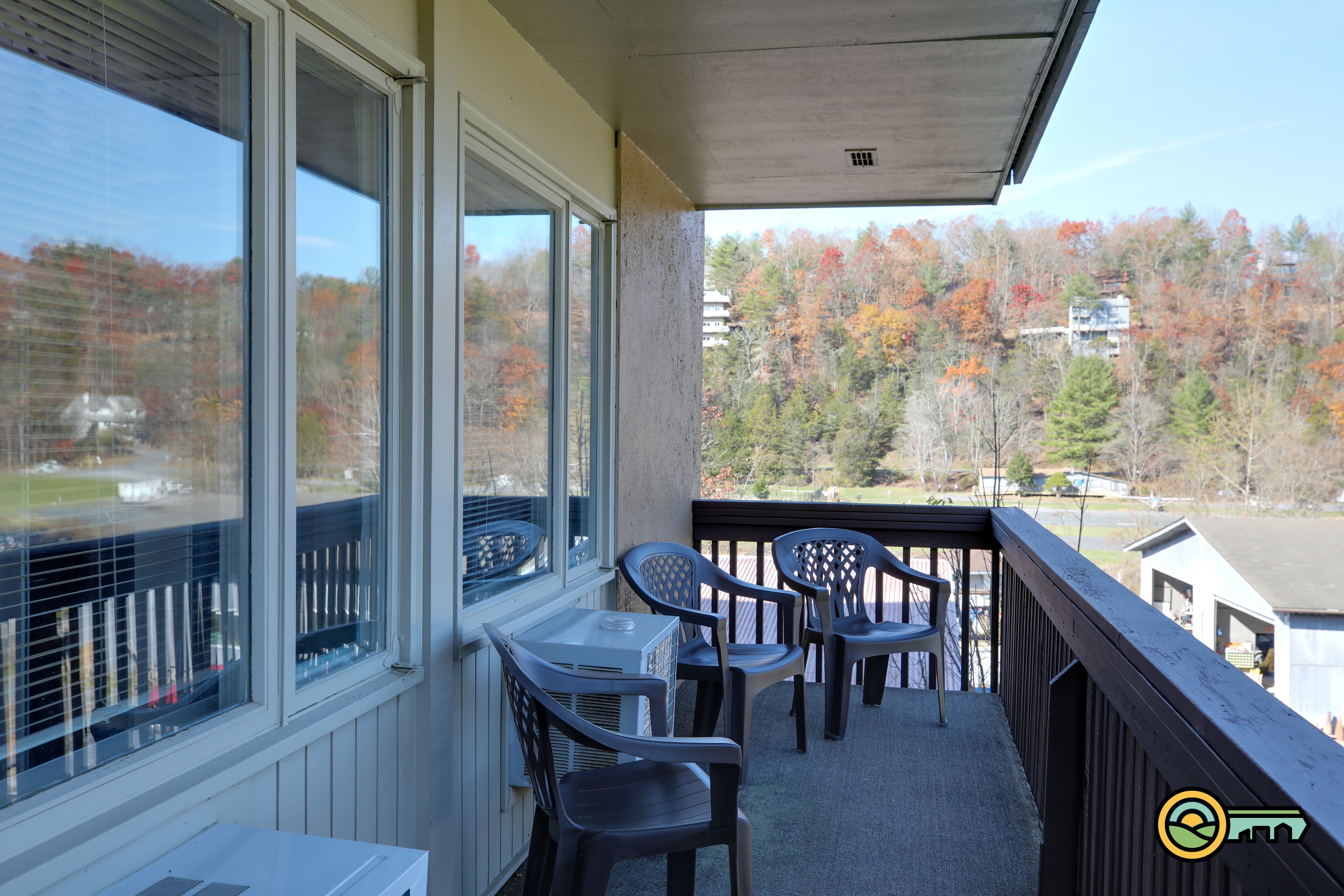 A balcony with a table and chairs, large windows, and a view of trees and buildings.