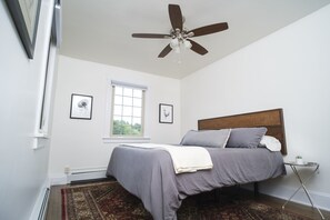 Cozy retreat with a large bed, ceiling fan, and a window overlooking lush greenery.
