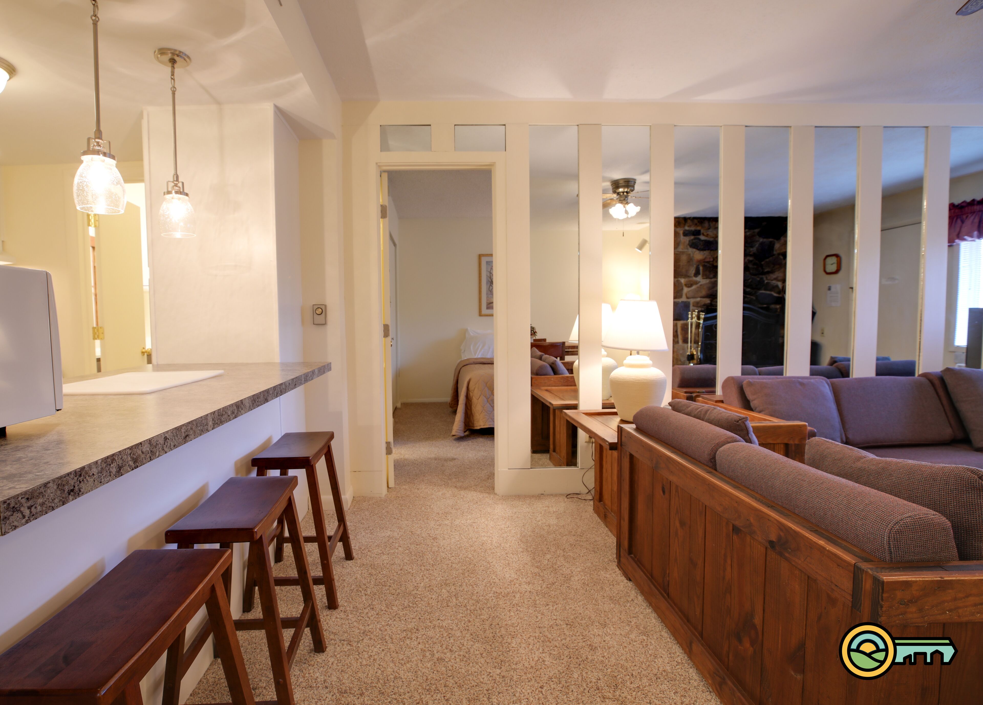 Una sala de estar acogedora con un banco de madera, un sofá y un comedor con mostrador y taburetes.