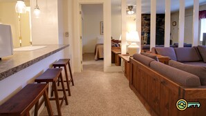 Un salon chaleureux avec un banc en bois, un canapé et un coin repas comprenant un comptoir et des tabourets.