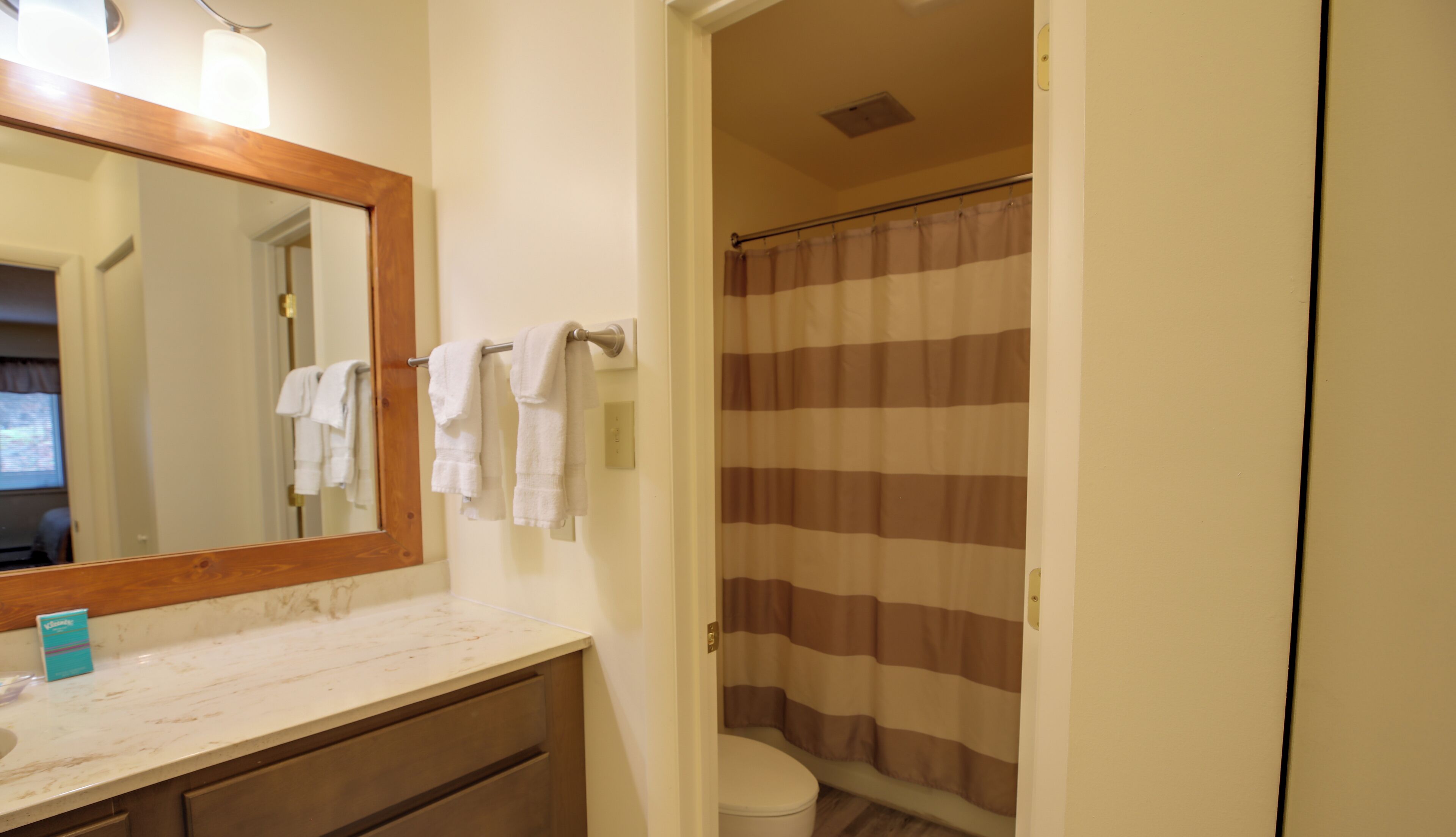 A bathroom with a wooden-framed mirror, a white sink, a towel rack with white towels, a striped shower curtain, and a toilet.
