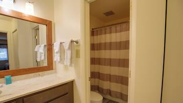 A bathroom with a wooden-framed mirror, a white sink, a towel rack with white towels, a striped shower curtain, and a toilet.