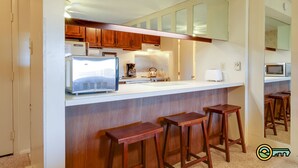 Una cocina con armarios de madera, microondas, tostadora y cafetera. Hay tres taburetes de madera en la encimera.