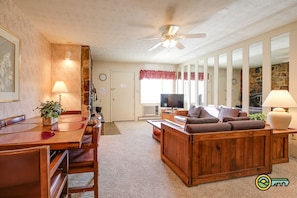 A cozy living room with a wooden coffee table, a sofa, and a television. There is a dining area with a table and chairs, and a stone wall in the background.