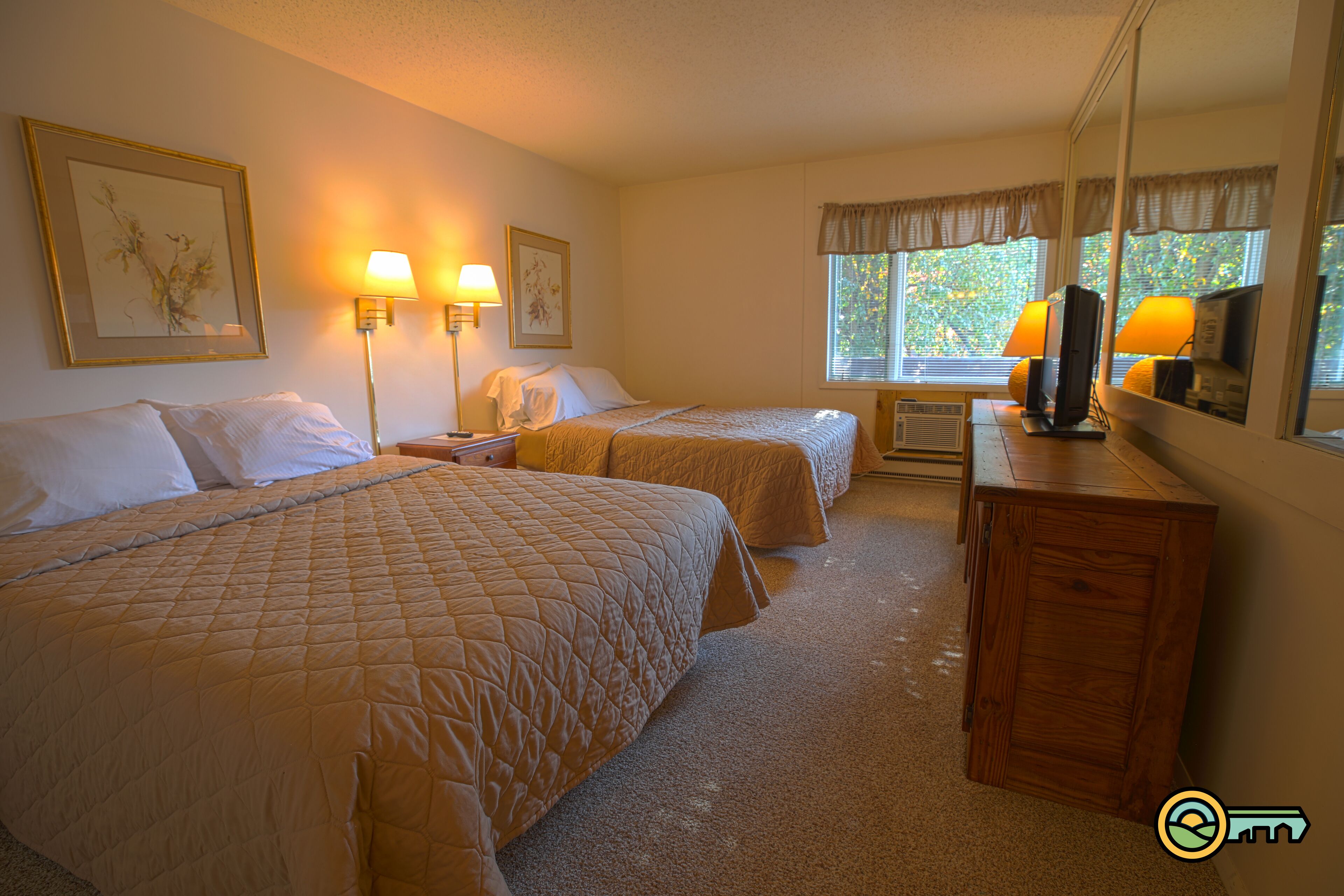 A hotel room with two beds, a desk, a mirror, and a window with curtains.