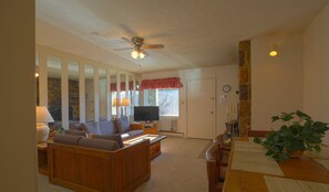 A living room with a sofa, TV, and a dining table with placemats. - Ski/MTB/Golf Condo (#128) - Slope side | Wonderful mountain & golf course views! (Basye)