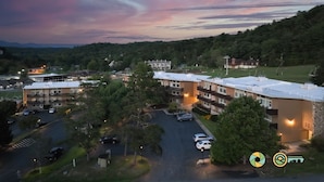 An aerial view of a multi-story building complex with parking areas, surrounded by greenery and a hilly landscape. - Ski/MTB/Golf Condo (#131) - Slope side | Slope & Resort valley views | Vaulted ceilings! (Basye)