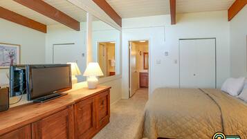 A bedroom with a bed, a TV on a wooden dresser, a mirror, and a door leading to a bathroom.