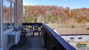 A balcony with a view of autumn trees, a window with blinds, and two chairs. - Ski/MTB/Golf Condo (#131) - Slope side | Slope & Resort valley views | Vaulted ceilings! (Basye)