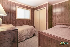 Un dormitorio con dos camas, un armario de madera, una ventana con persianas y una lámpara sobre una mesita de noche.