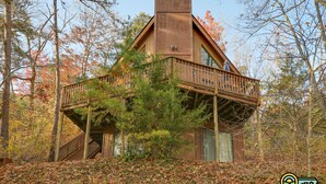 A cabin with a wooden exterior, a balcony, and a staircase leading to the entrance.