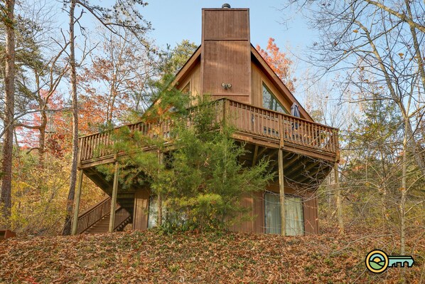 A cabin with a wooden exterior, a balcony, and a staircase leading to the entrance.