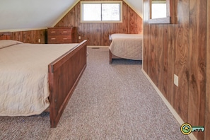 A bedroom with two beds, wooden walls, a window, and a carpeted floor.