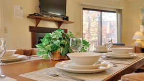 Un tavolo da pranzo apparecchiato con piatti, ciotole e posate, una televisione sopra e una finestra con foglie autunnali.
