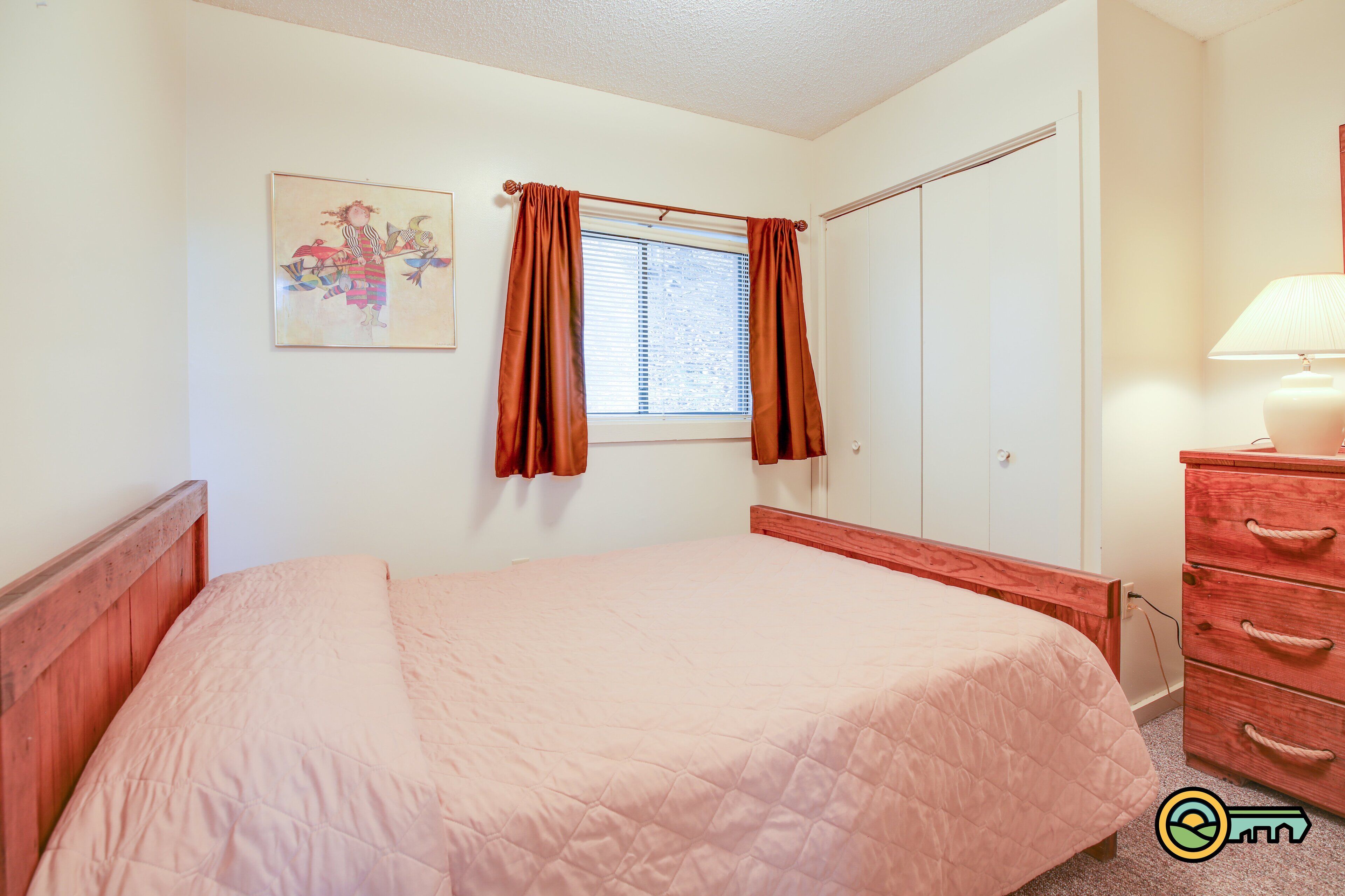 A bedroom with a bed, a dresser, a nightstand, a window with curtains, and a painting on the wall.