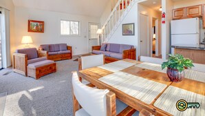 A spacious living area with a wooden dining table, cushioned seating, and a staircase leading to an upper level. - Cozy Mountain Chalet (#102) - Quiet location | Summertime secluded | Great winter views! (Basye)